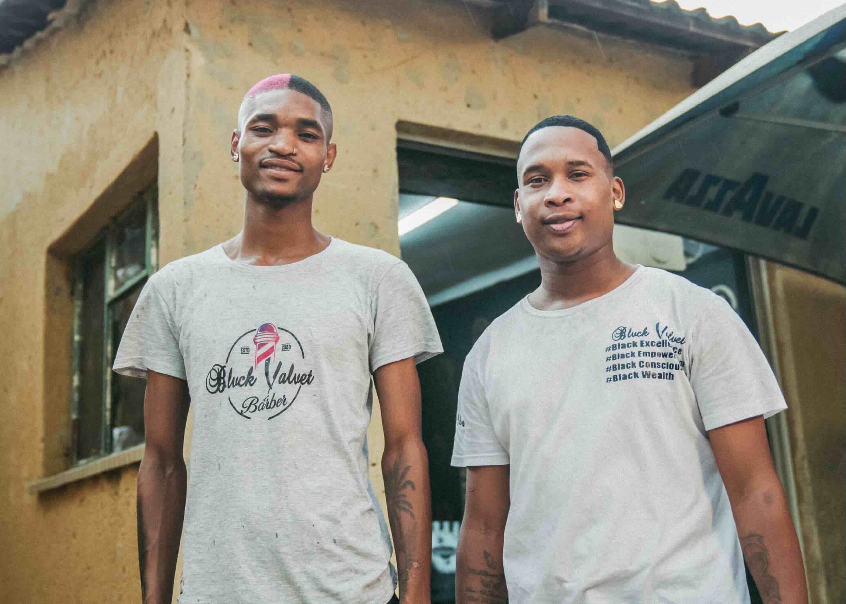 Two men standing outside a building, both wearing t-shirts with the logo 'Black Valvet Barber'.