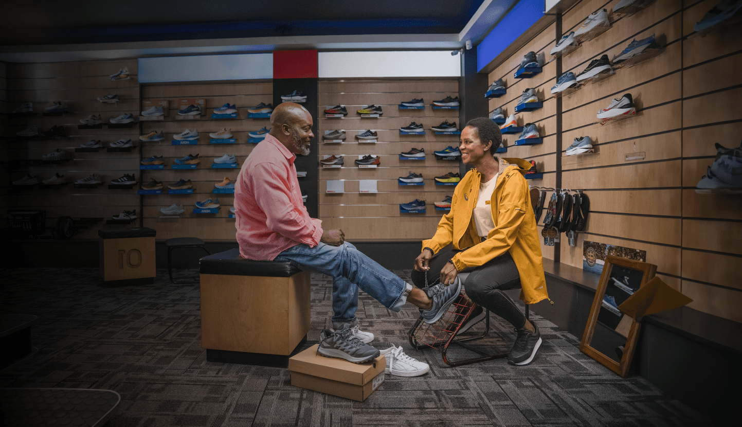 Sales assistant helping a customer try on sneakers in a shoe store.